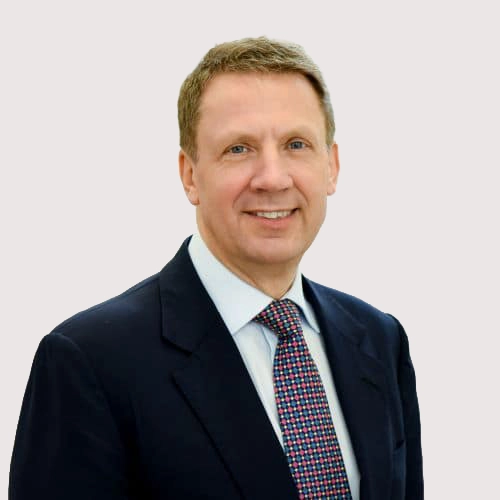 Portrait of a middle-aged man in a suit and patterned tie, smiling at the camera against a plain background.